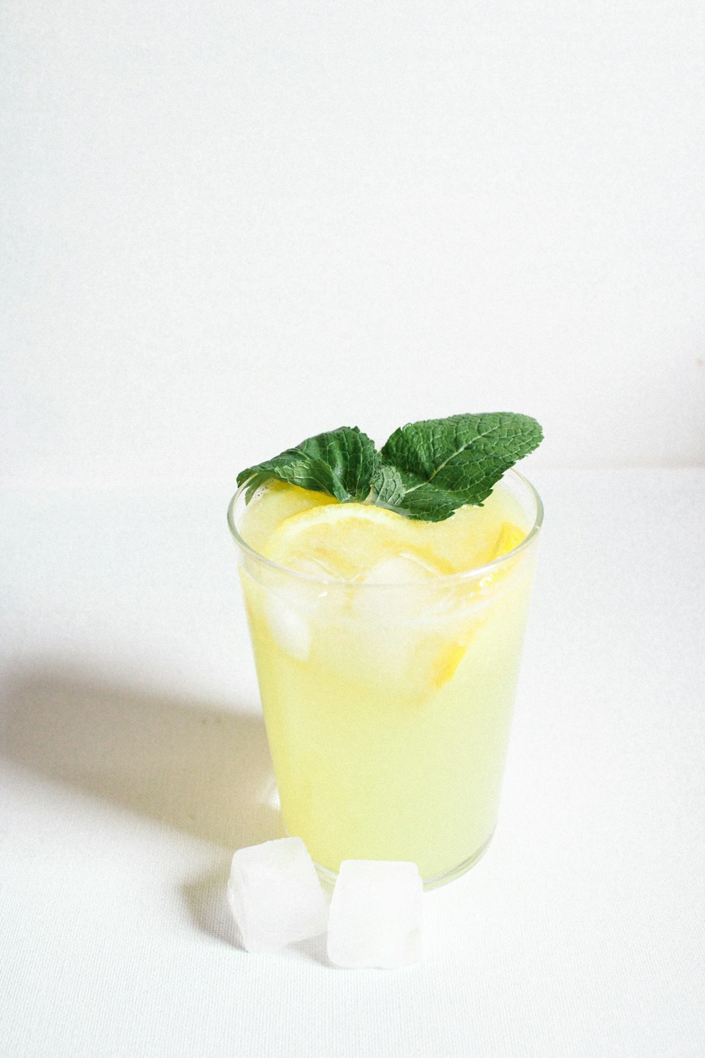 clear drinking glass with yellow liquid and green leaf