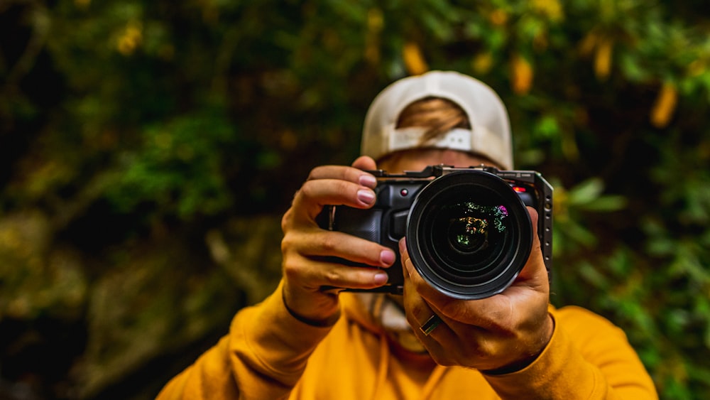 Persona con camisa amarilla de manga larga sosteniendo una cámara DSLR Nikon negra