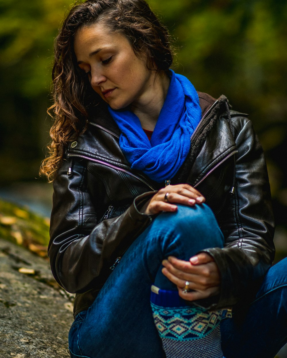 woman in black leather jacket and blue denim jeans sitting on ground during daytime