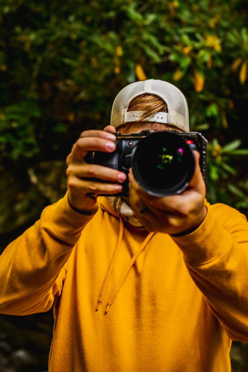 黒いデジタル一眼レフカメラで写真を撮る黄色のパーカーを着た男