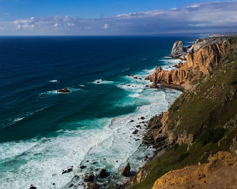 brown rocky mountain beside blue sea during daytime