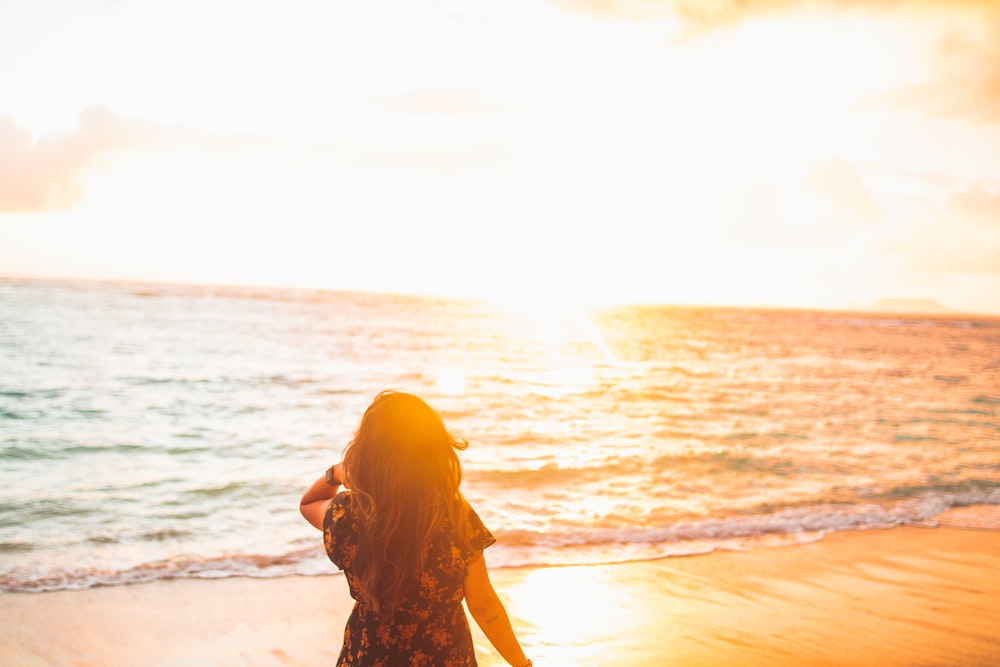 woman in black and brown floral dress standing on seashore during sunset