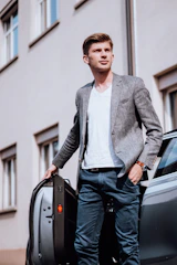A smartly dressed chauffeur opening a car door for a passenger in a busy Chennai street.
