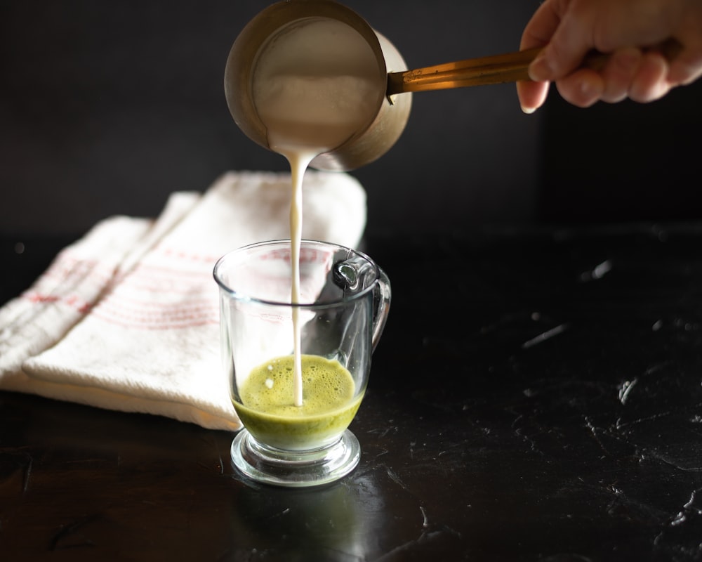 person pouring milk on clear drinking glass