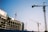 Multiple construction cranes are visible at a building site. A partially constructed building appears to the left, with cranes extended into the sky. The blue sky provides a clear backdrop, emphasizing the scale and complexity of the construction process.