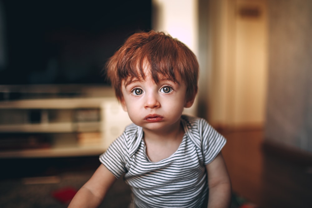 boy in white and black striped crew neck t-shirt sitting on brown wooden table