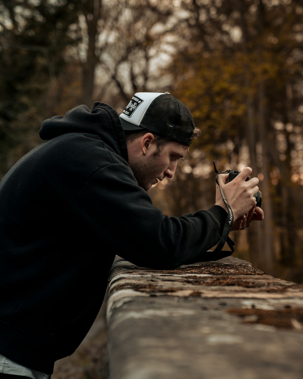 man in black jacket and black cap sitting on brown wooden log during daytime