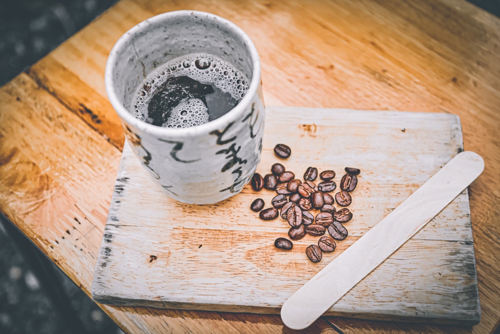 white and black ceramic mug on brown wooden chopping board