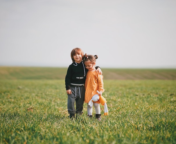 woman in black long sleeve shirt holding girl in orange dress on green grass field during