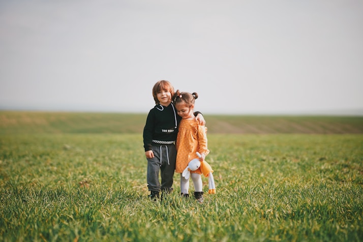 woman in black long sleeve shirt holding girl in orange dress on green grass field during