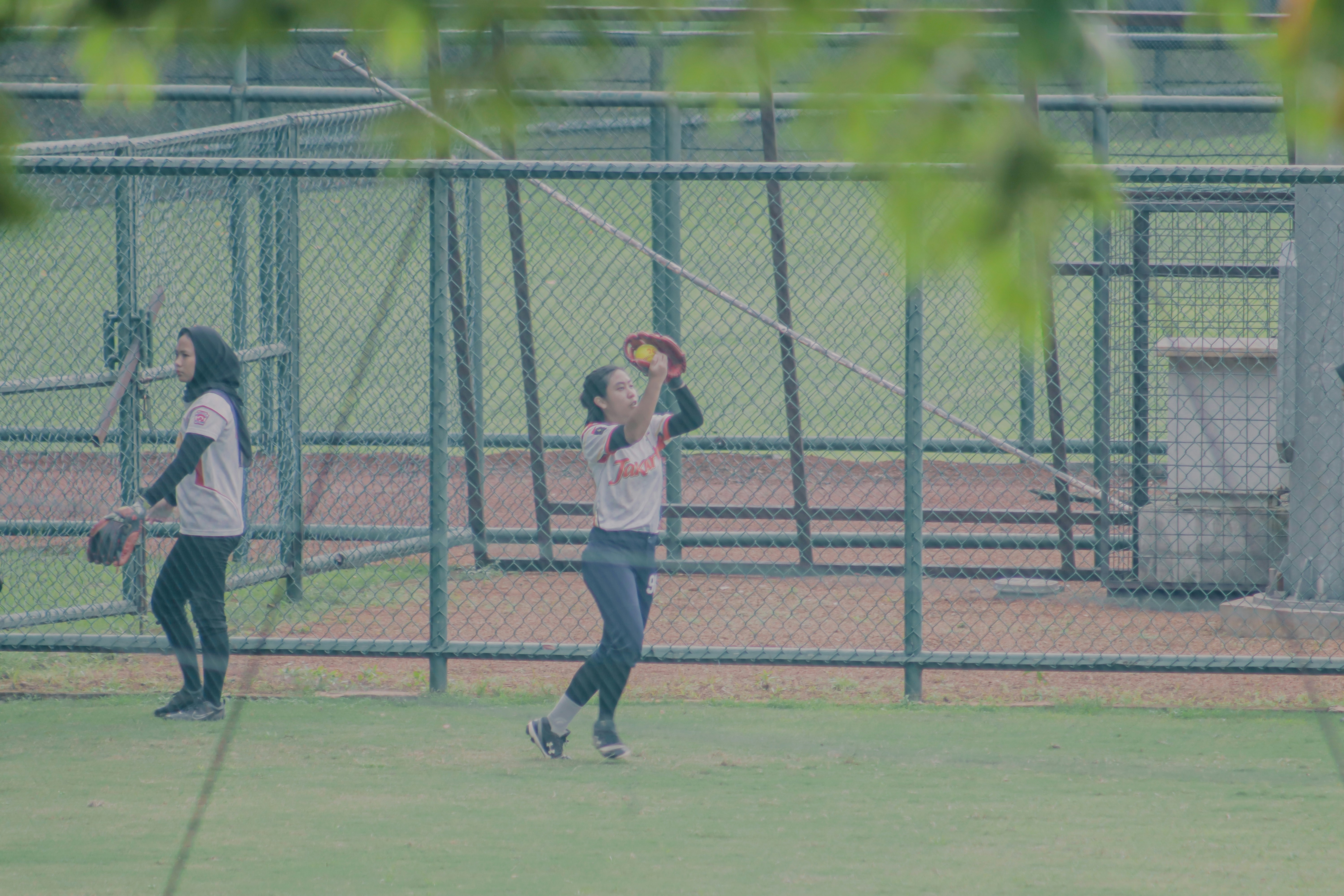 Young girls learning to catch a softball, bright sunny field, coaches kneeling beside them