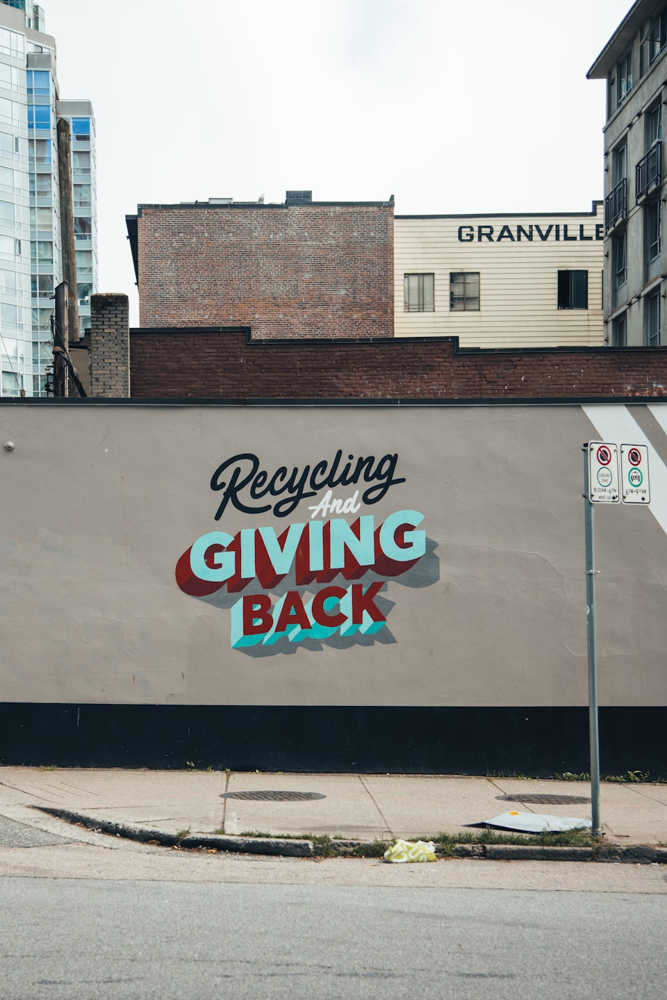 A wall next to a street with the text, "Recycling and GIVING BACK".