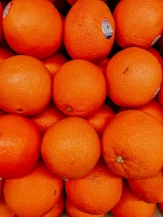A pile of fresh oranges closely packed together, with a bright and vibrant orange color. Some oranges have small labels on them.