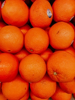 A pile of fresh oranges closely packed together, with a bright and vibrant orange color. Some oranges have small labels on them.