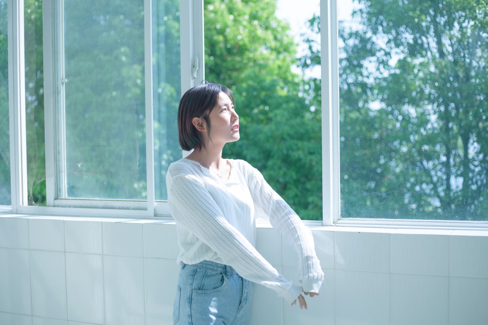 woman in white long sleeve shirt and blue denim jeans standing by the window