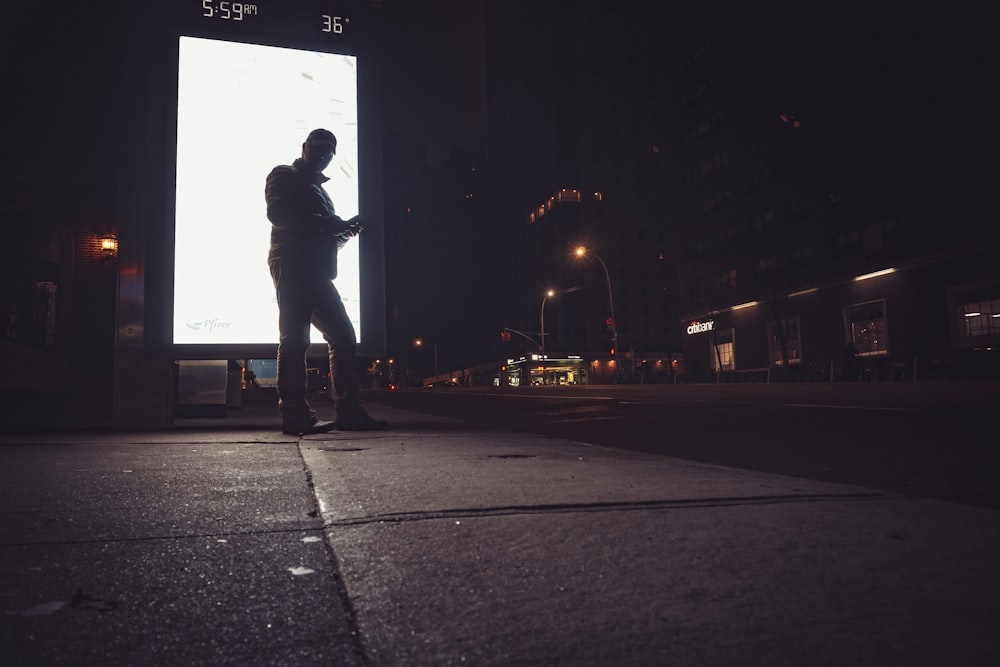 man in black jacket and blue denim jeans standing on gray concrete road during night time