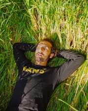 man in black long sleeve shirt lying on green grass field during daytime