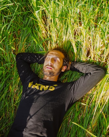 man in black long sleeve shirt lying on green grass field during daytime