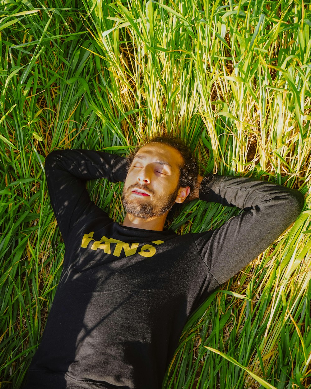 man in black long sleeve shirt lying on green grass field during daytime