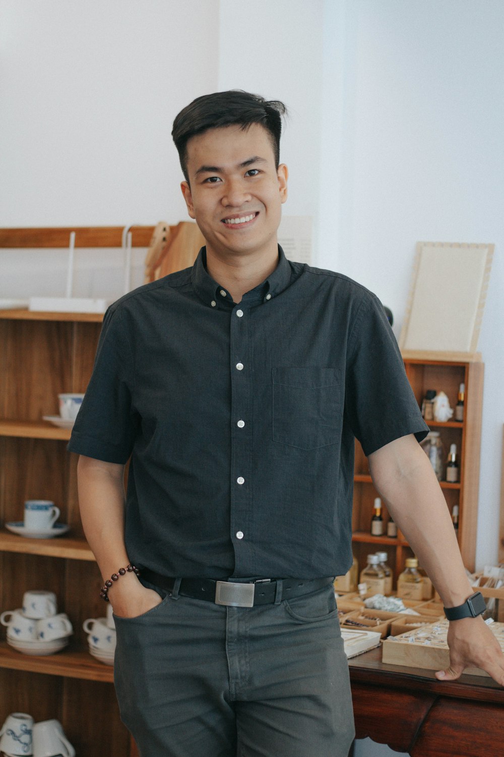 man in black button up shirt standing near brown wooden shelf