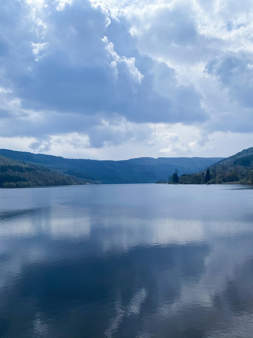 body of water near green mountains under white clouds and blue sky during daytime