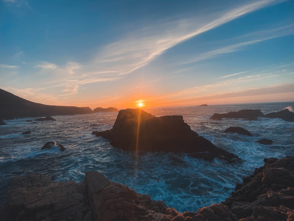 black rock formation on sea during sunset