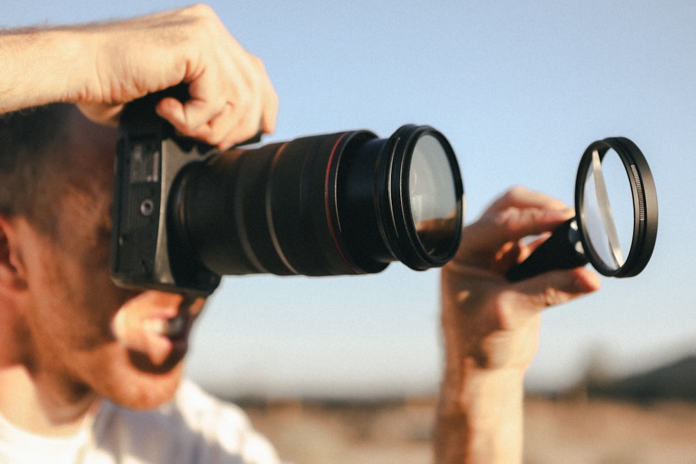 man in white crew neck shirt holding black dslr camera