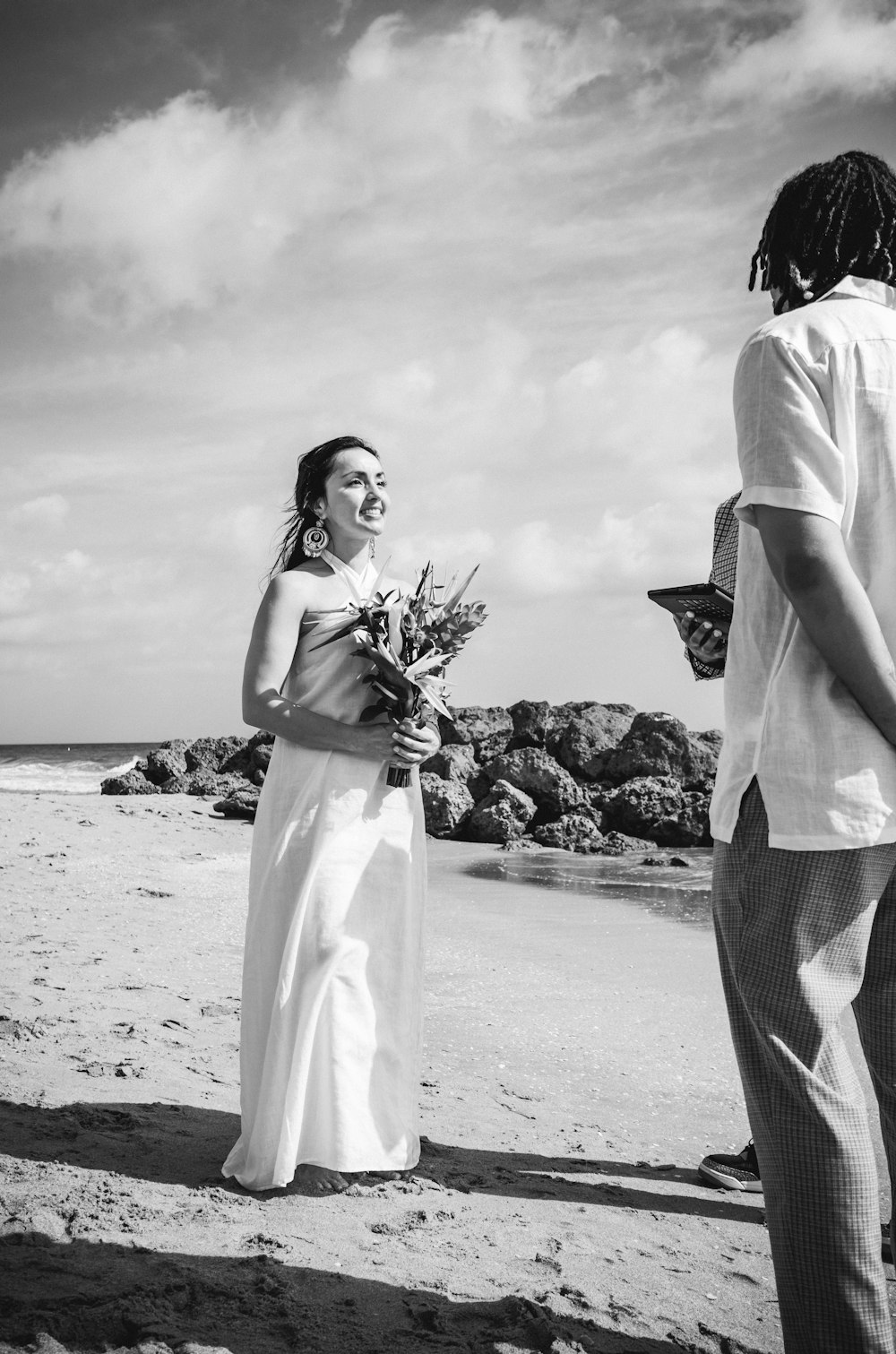 woman in white dress holding bouquet of flowers standing on beach