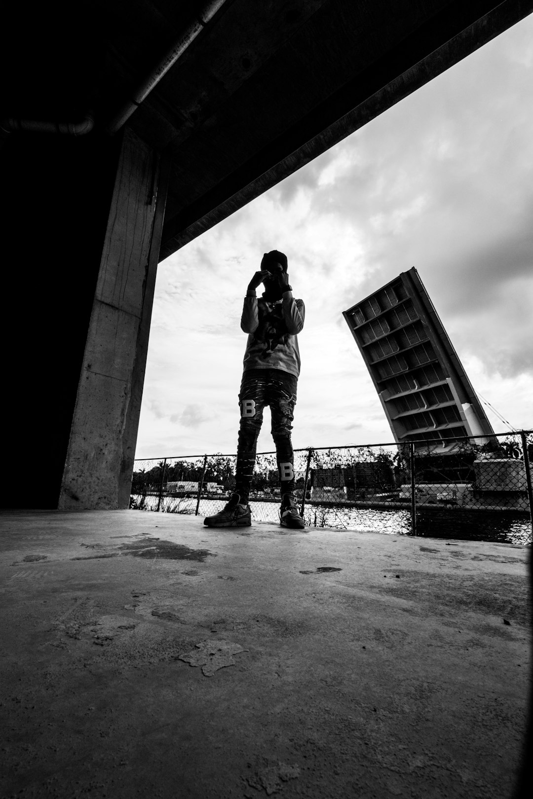 grayscale photo of man in black jacket and pants standing on concrete floor