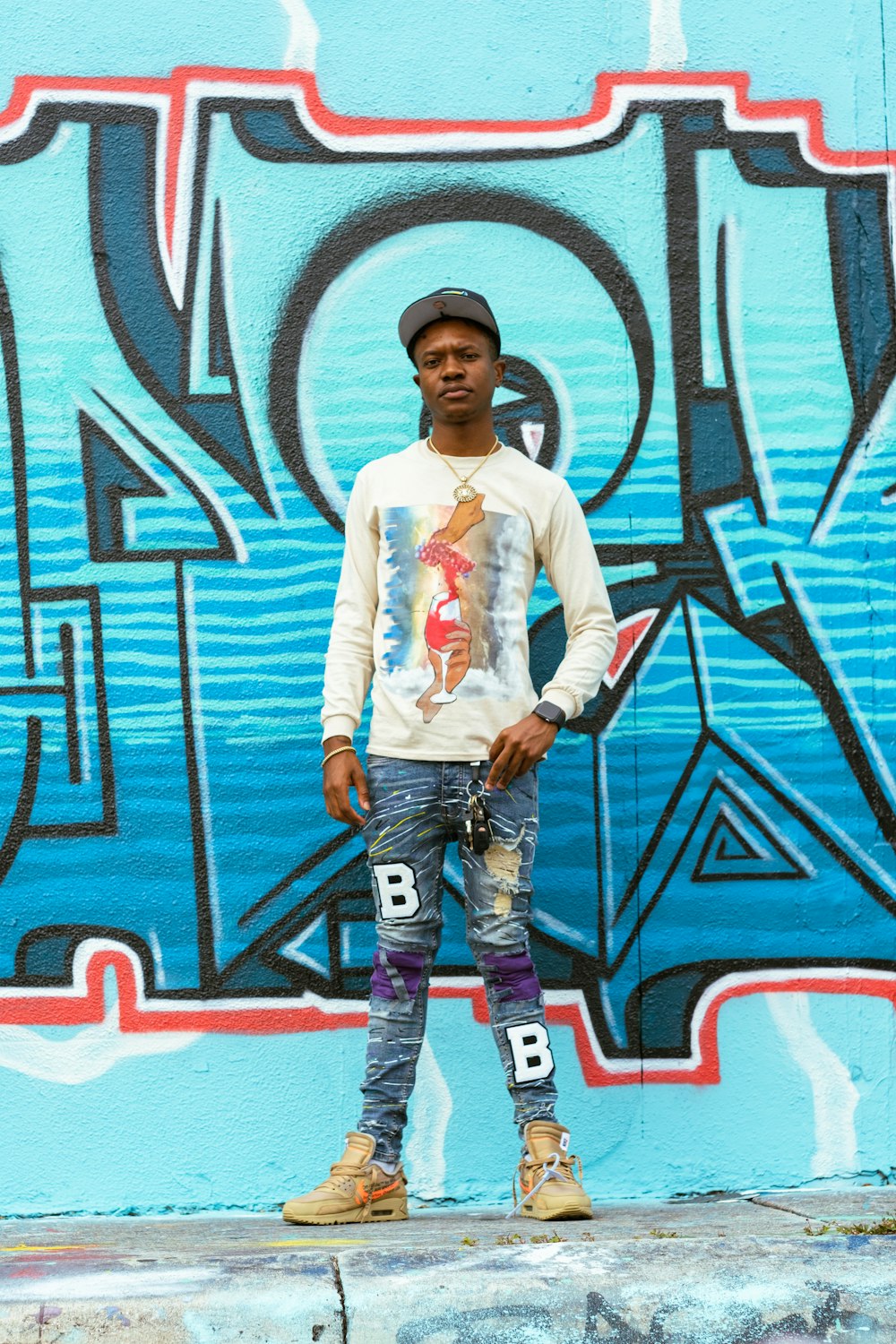 man in white dress shirt and blue denim jeans standing beside wall with graffiti during daytime