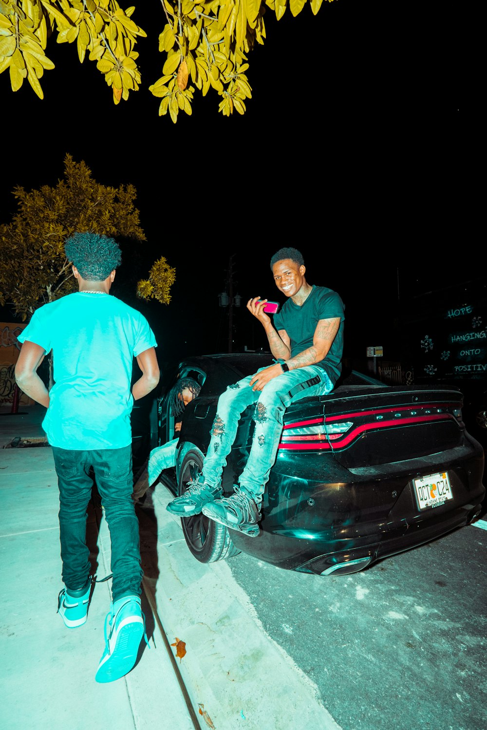 man in blue t-shirt and blue denim jeans standing beside black car during night time