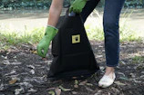 Close-up of a gloved hand carefully picking up dog waste with eco-friendly bags in a shaded neighborhood.