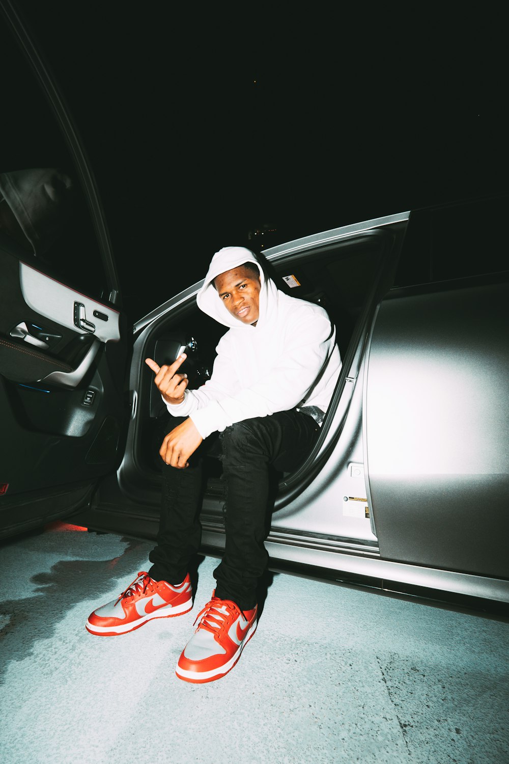 man in white hoodie and black pants sitting on car