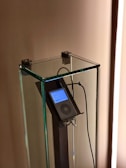 An iPod is encased in a transparent glass display stand, mounted on a metallic holder. Earphones are connected to the iPod, which displays a list on its screen.