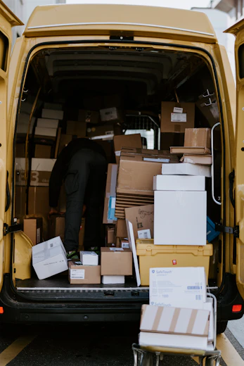 A person in dark clothing loading cardboard boxes into a yellow delivery van
