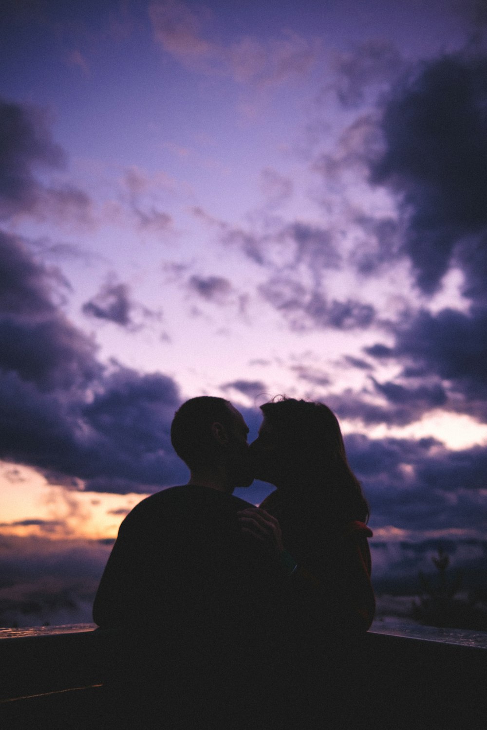silhueta do homem e da mulher que se beijam sob o céu nublado durante o dia
