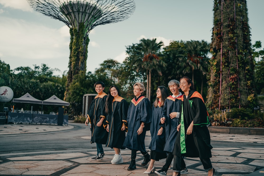 Gruppo di persone in abito accademico nero in piedi sul marciapiede di cemento grigio durante il giorno