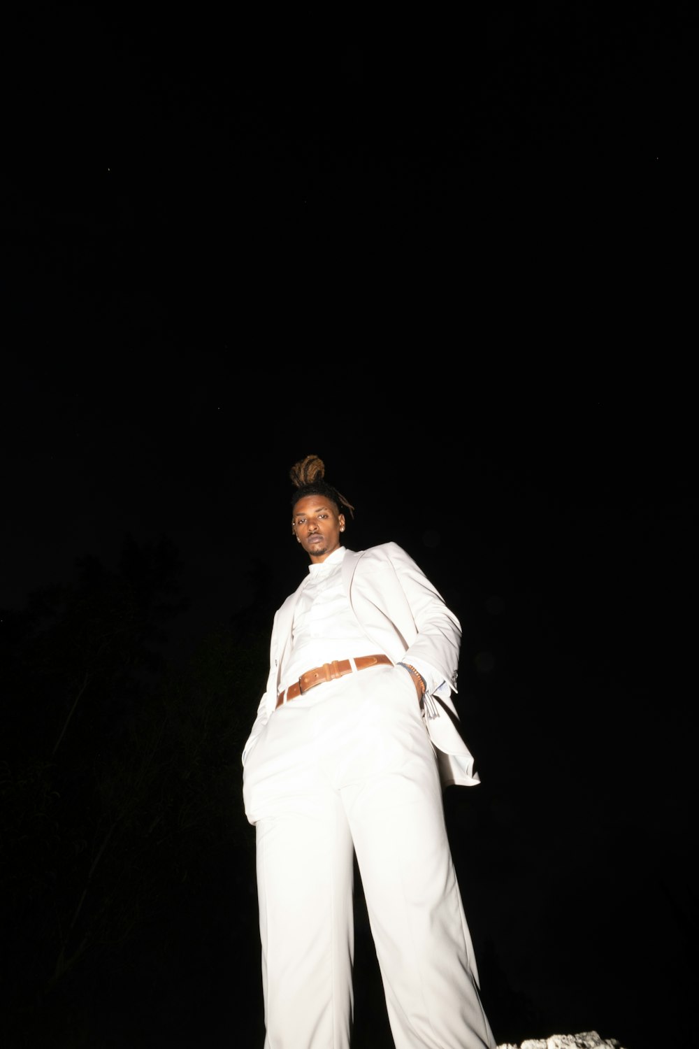 man in white long sleeve shirt and white pants standing on black background