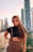 A confident escort walking along a scenic Dubai marina at sunset.