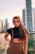 A confident escort walking along a scenic Dubai marina at sunset.