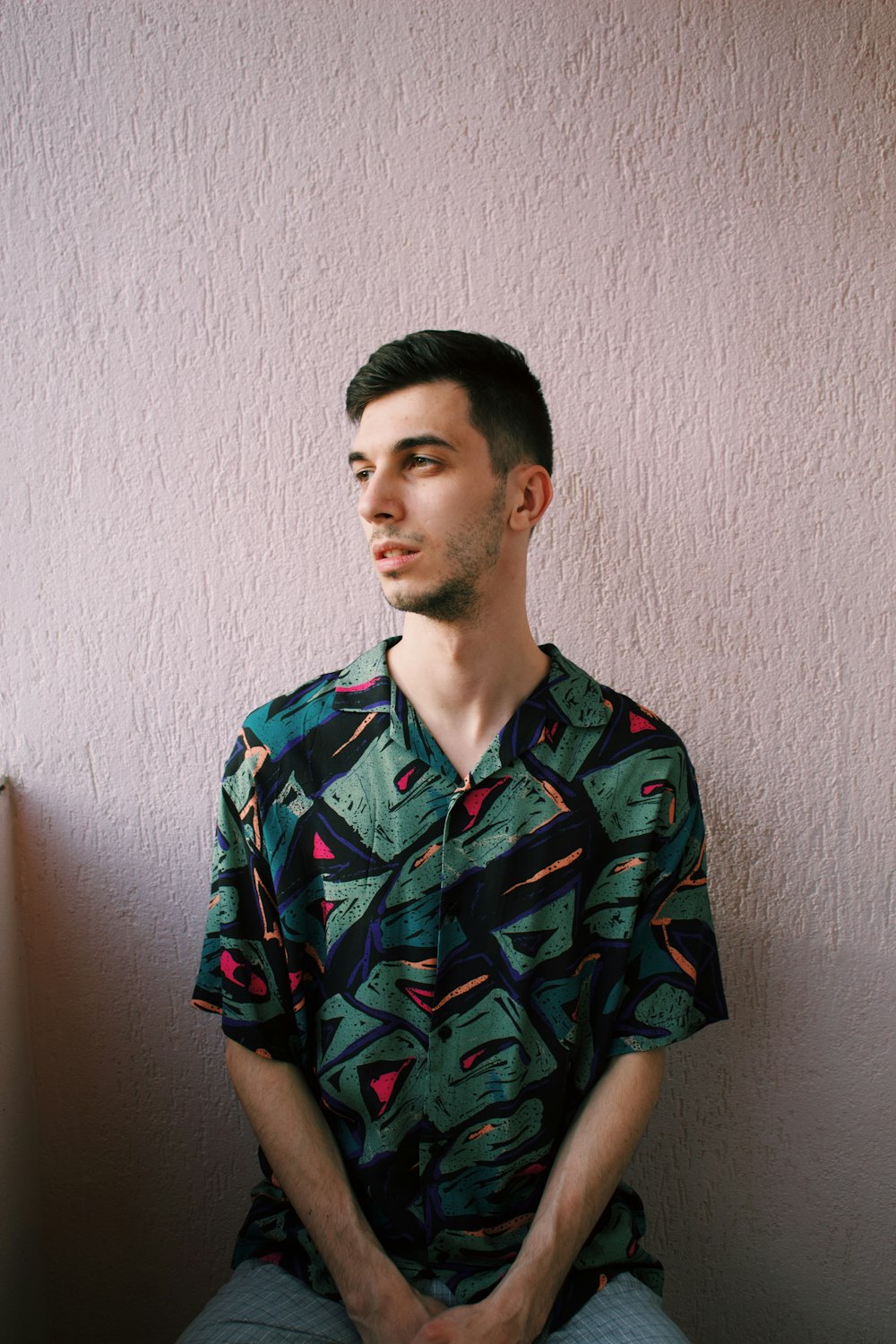 man in blue and red button up shirt standing beside white wall