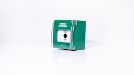 A green emergency door release box with a white front panel and a button labeled 'Press Here'. The box appears to be made of plastic and is set against a plain white background.