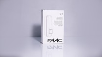 A product packaging box with a white background displaying the brand name 'FAAC' and the text 'Adjustable Photocells' along with translations in multiple languages. The image features clean lines and a minimalistic design with the CE certification mark visible.