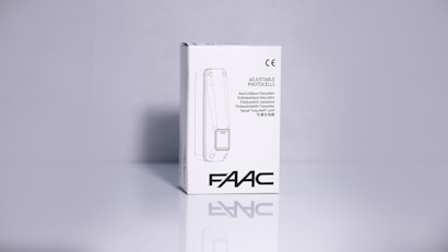 A product packaging box with a white background displaying the brand name 'FAAC' and the text 'Adjustable Photocells' along with translations in multiple languages. The image features clean lines and a minimalistic design with the CE certification mark visible.