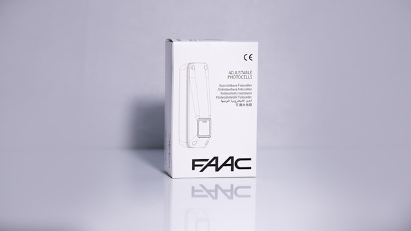 A product packaging box with a white background displaying the brand name 'FAAC' and the text 'Adjustable Photocells' along with translations in multiple languages. The image features clean lines and a minimalistic design with the CE certification mark visible.