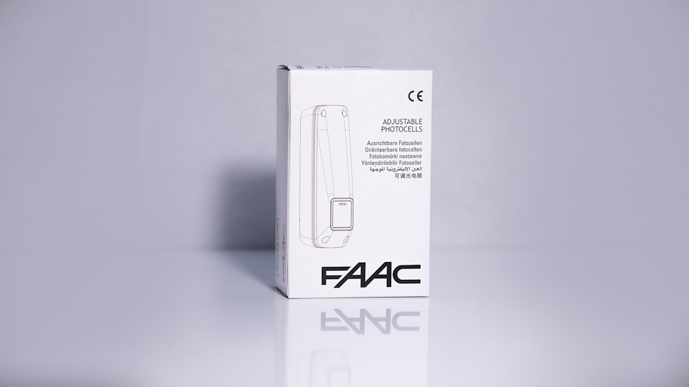 A product packaging box with a white background displaying the brand name 'FAAC' and the text 'Adjustable Photocells' along with translations in multiple languages. The image features clean lines and a minimalistic design with the CE certification mark visible.