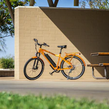 A vibrant electric bike leaning against a blue wall under bright sunlight.