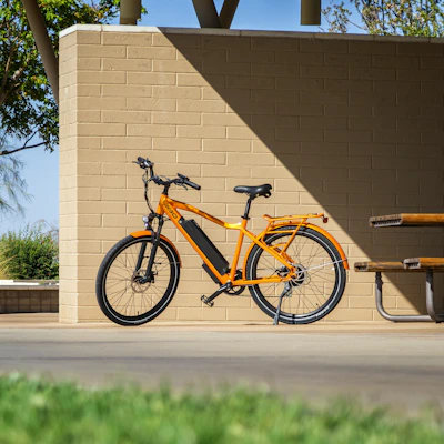 A vibrant electric bike leaning against a blue wall under bright sunlight.