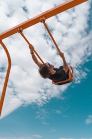 girl in black shirt and blue denim jeans riding on orange swing under blue and white