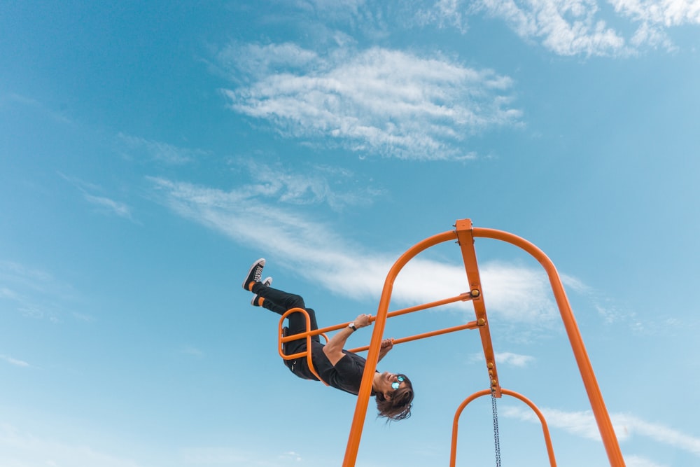 man in black jacket riding orange and black roller coaster under blue sky during daytime